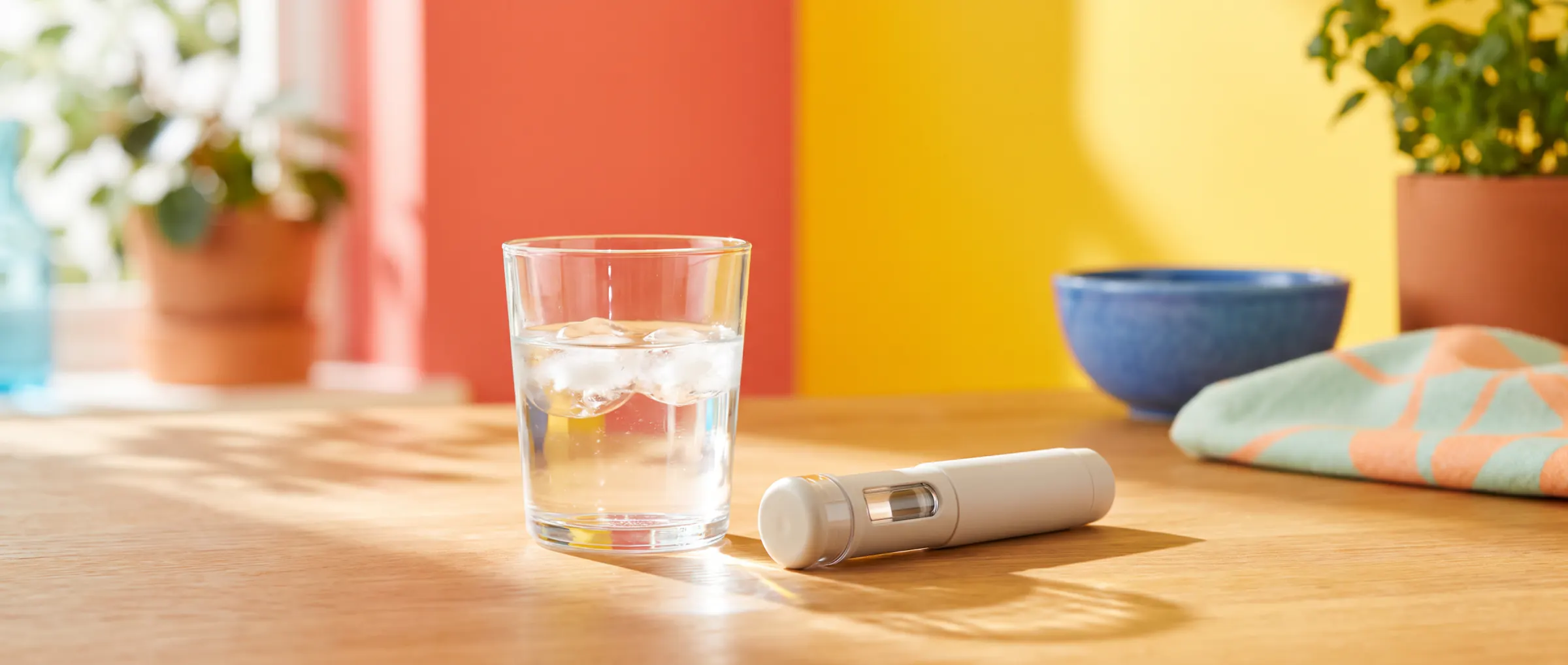 A half-full glass of water beside a plain injection pen in bright sunlight